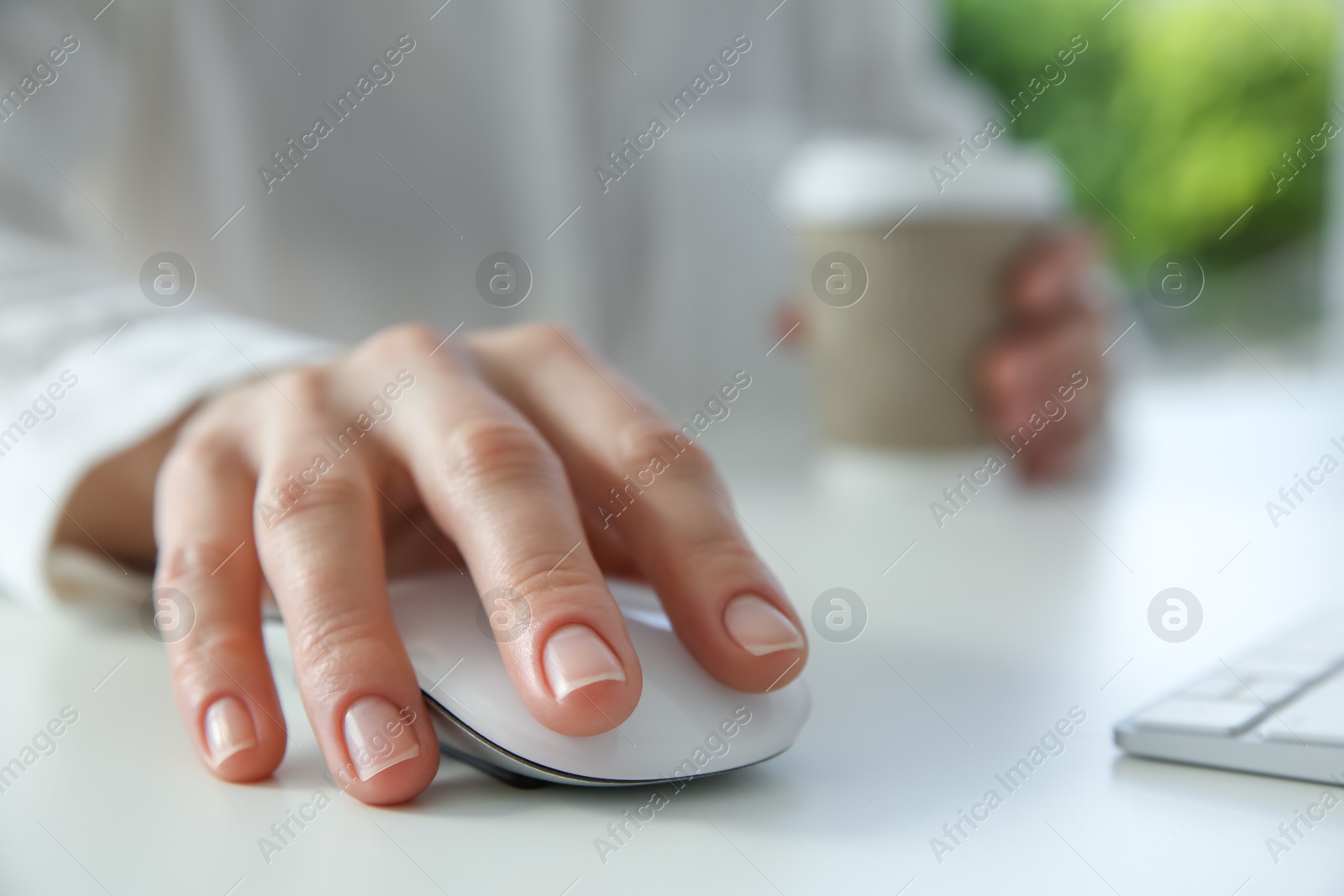 Photo of Woman with wireless mouse and paper cup at white table indoors, closeup