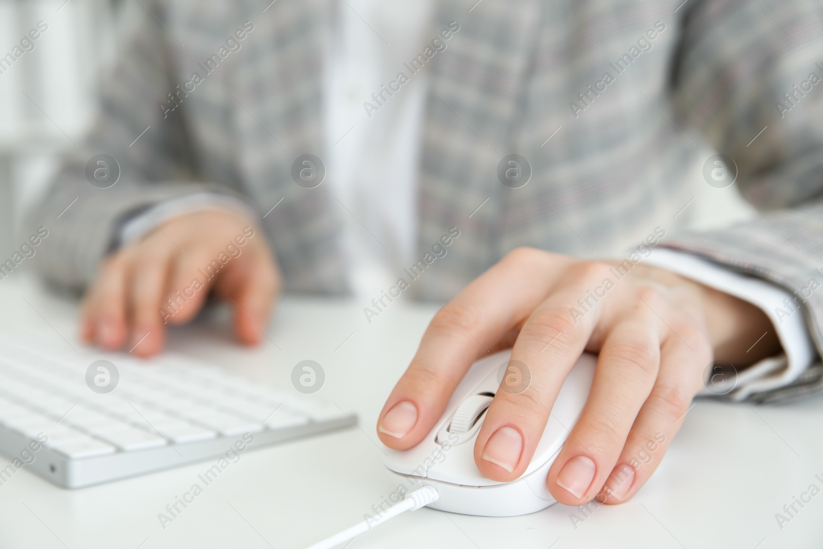 Photo of Woman working with wired mouse and computer keyboard at white table indoors, closeup