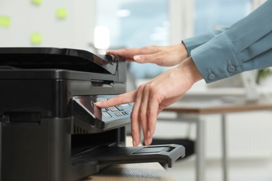 Photo of Woman using modern printer at workplace indoors, closeup