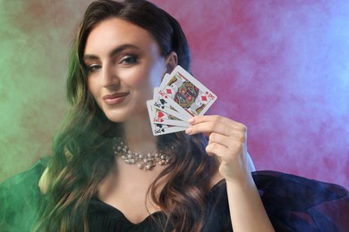 Photo of Poker game. Charming woman with playing cards on red background in color lights and smoke