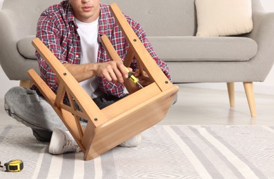 Man repairing wooden stool with screwdriver indoors, closeup