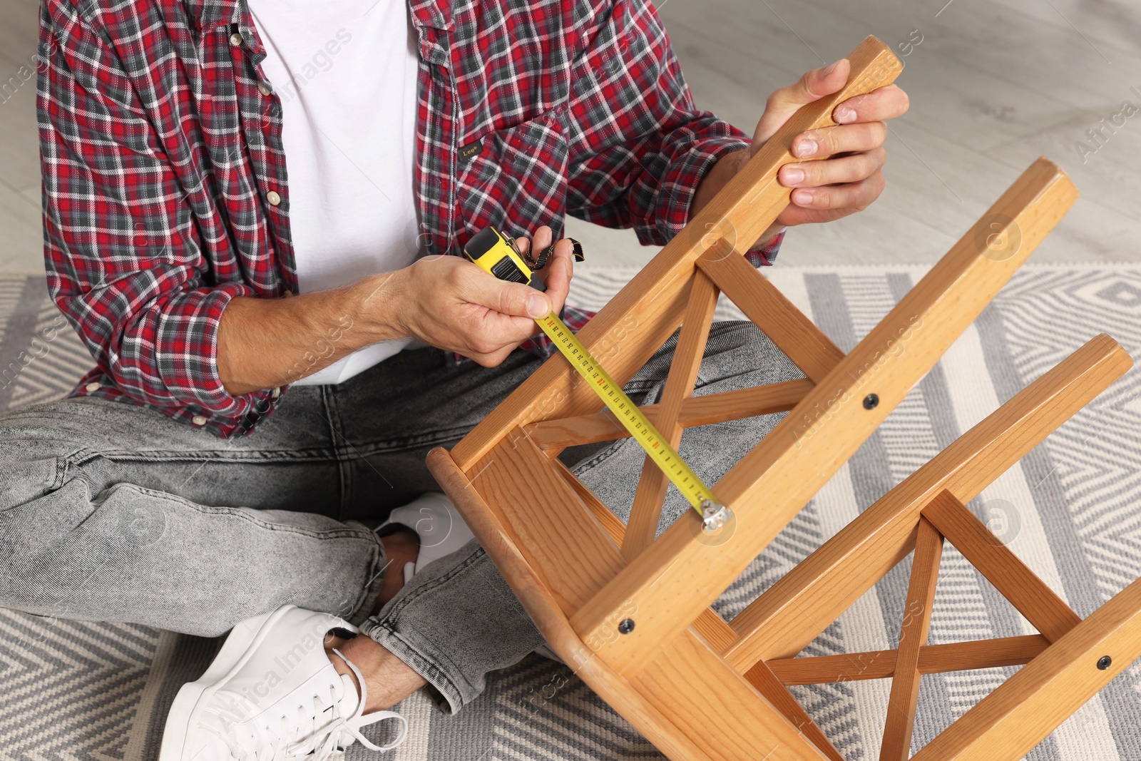 Photo of Man using tape measure while repairing wooden stool indoors, closeup