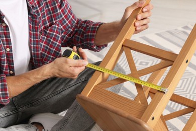 Photo of Man using tape measure while repairing wooden stool indoors, closeup