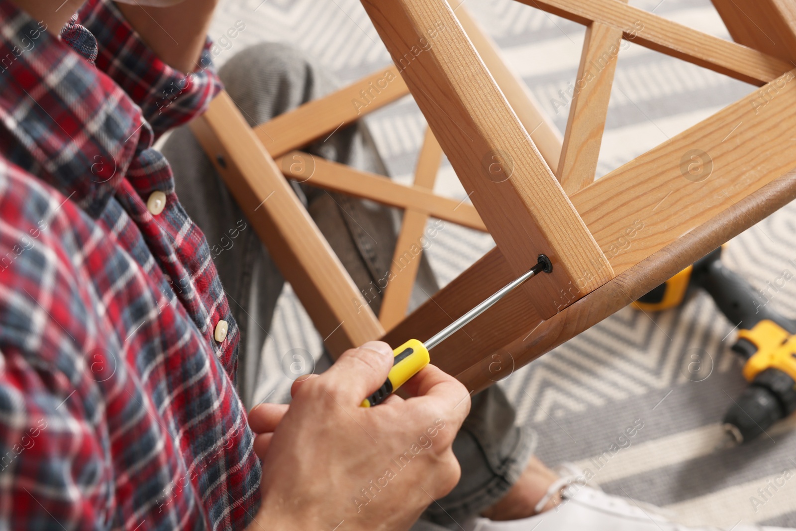 Photo of Man repairing wooden stool with screwdriver indoors, closeup