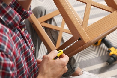 Photo of Man repairing wooden stool with screwdriver indoors, closeup