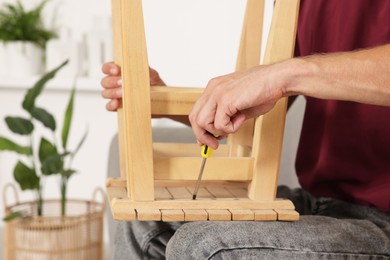 Man repairing wooden stool with screwdriver indoors, closeup