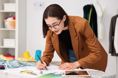 Photo of Fashion designer drawing sketch of dress at table in workshop