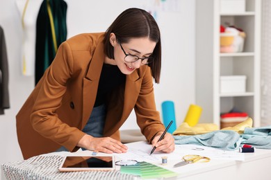 Photo of Fashion designer drawing sketch of dress at table in workshop