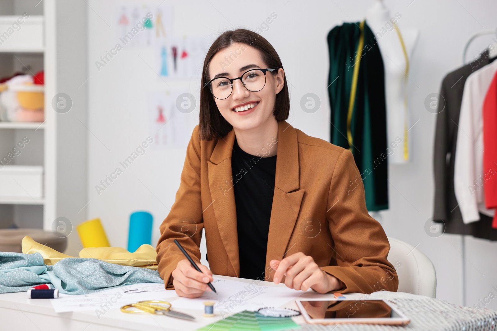 Photo of Fashion designer drawing sketch of dress at table in workshop