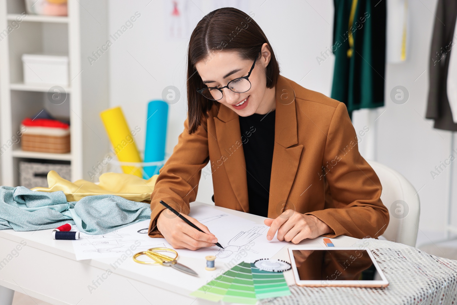 Photo of Fashion designer drawing sketch of dress at table in workshop