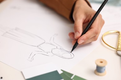 Photo of Fashion designer drawing sketch of dress at table, closeup