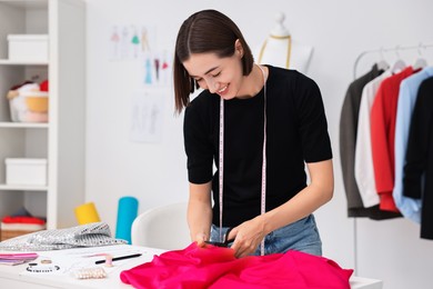 Photo of Fashion designer cutting pink fabric at table in workshop