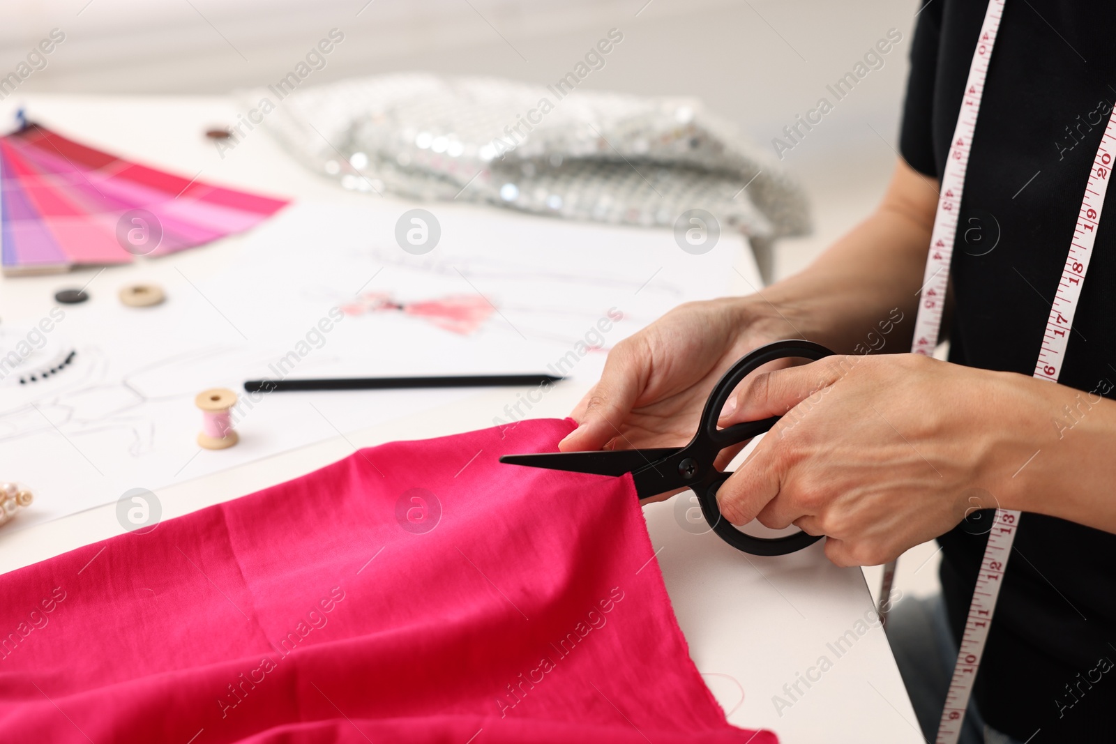 Photo of Fashion designer cutting pink fabric at table in workshop, closeup