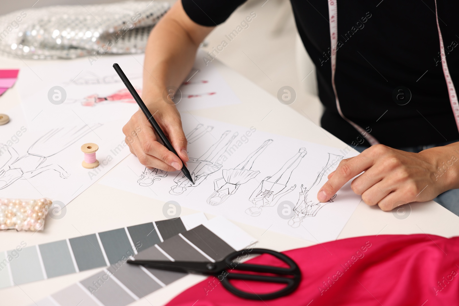 Photo of Fashion designer drawing sketch of beautiful outfit at table in workshop, closeup