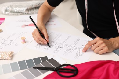 Photo of Fashion designer drawing sketch of beautiful outfit at table in workshop, closeup