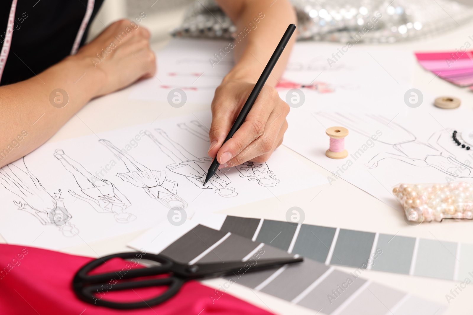 Photo of Fashion designer drawing sketch of beautiful outfit at table in workshop, closeup