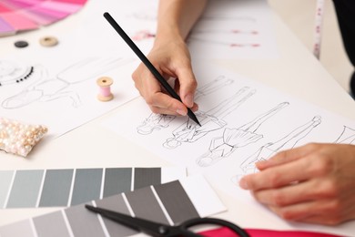 Photo of Fashion designer drawing sketch of beautiful outfit at table in workshop, closeup