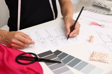 Photo of Fashion designer drawing sketch of beautiful outfit at table in workshop, closeup