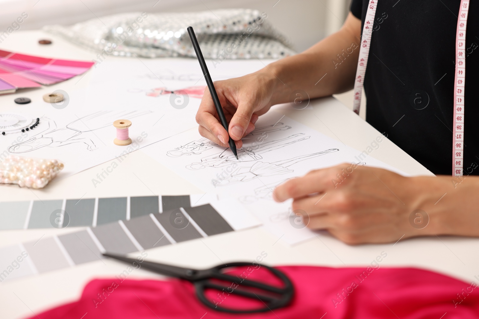 Photo of Fashion designer drawing sketch of beautiful outfit at table in workshop, closeup