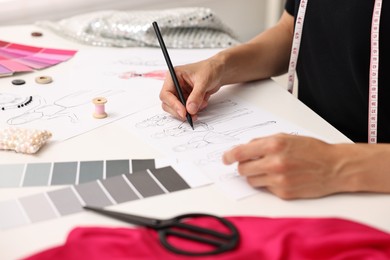 Fashion designer drawing sketch of beautiful outfit at table in workshop, closeup