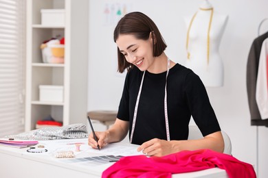 Fashion designer drawing sketch of beautiful outfit at table in workshop