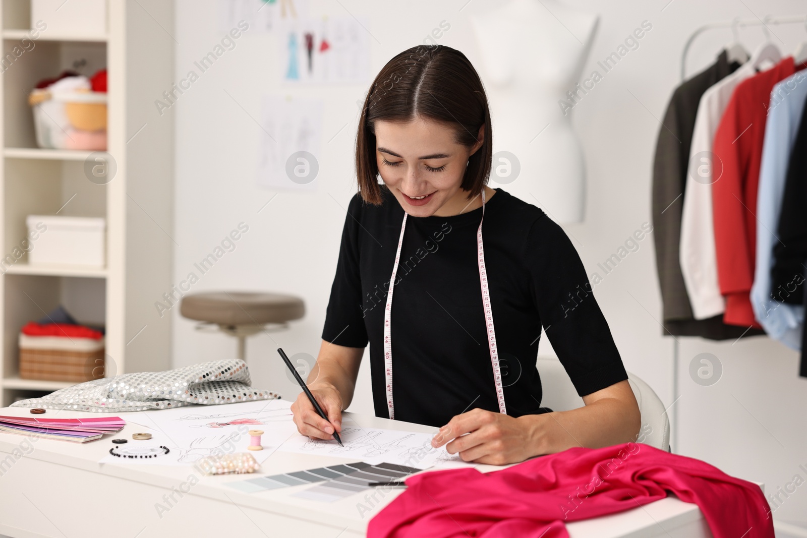 Photo of Fashion designer drawing sketch of beautiful outfit at table in workshop