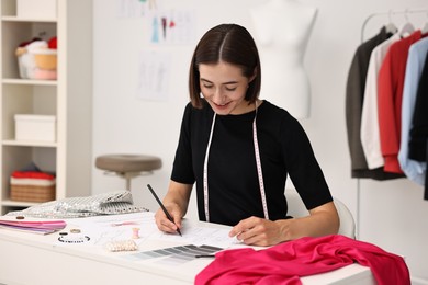 Photo of Fashion designer drawing sketch of beautiful outfit at table in workshop