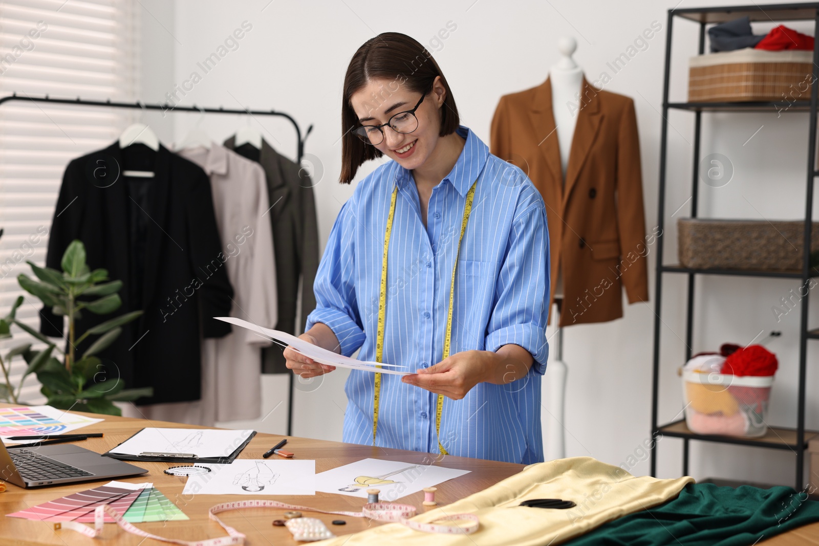 Photo of Fashion designer with sketches at wooden table in workshop