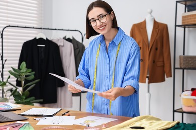 Photo of Fashion designer with sketches at wooden table in workshop