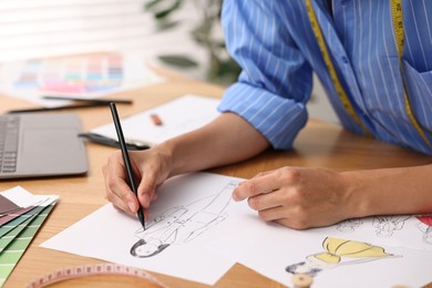 Photo of Fashion designer drawing sketch of beautiful outfit at wooden table, closeup