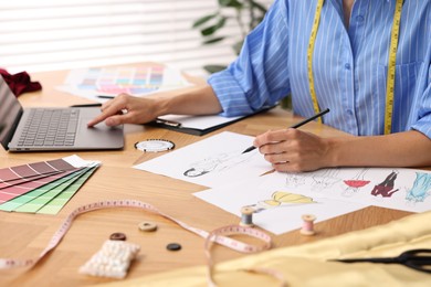 Photo of Fashion designer drawing sketch of beautiful outfit at wooden table, closeup