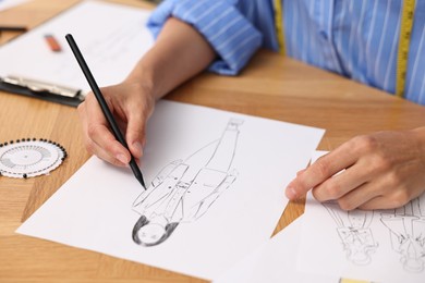 Photo of Fashion designer drawing sketch of beautiful outfit at wooden table, closeup