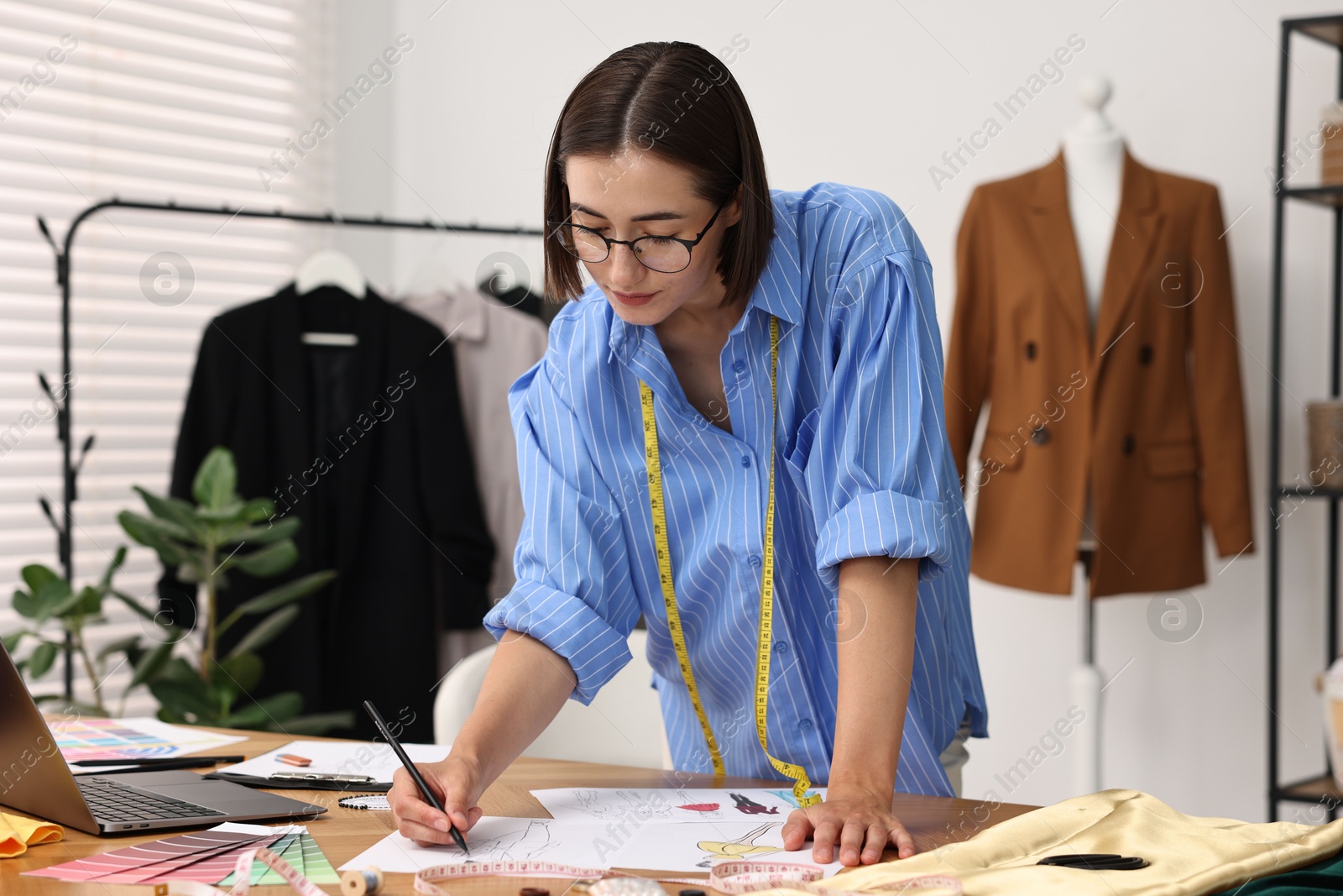 Photo of Fashion designer drawing sketch of beautiful outfit at wooden table in workshop