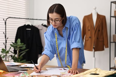 Fashion designer drawing sketch of beautiful outfit at wooden table in workshop