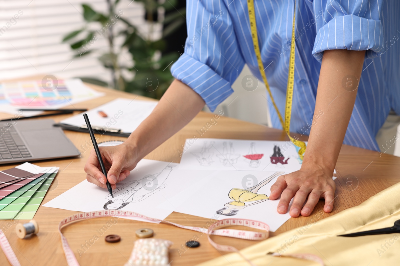 Photo of Fashion designer drawing sketch of beautiful outfit at wooden table, closeup