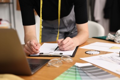 Photo of Fashion designer drawing sketch of beautiful outfit at wooden table, closeup