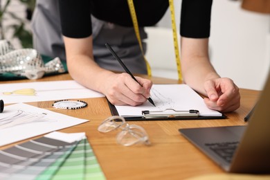 Photo of Fashion designer drawing sketch of beautiful outfit at wooden table, closeup