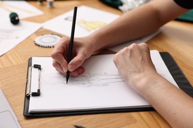 Photo of Fashion designer drawing sketch of beautiful outfit at wooden table, closeup