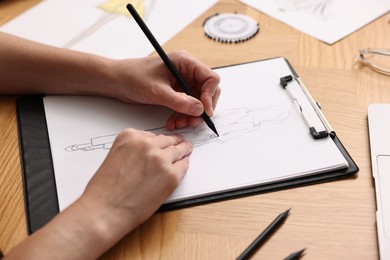 Photo of Fashion designer drawing sketch of beautiful outfit at wooden table, closeup