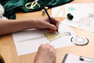 Fashion designer drawing sketch of beautiful dress at wooden table, closeup