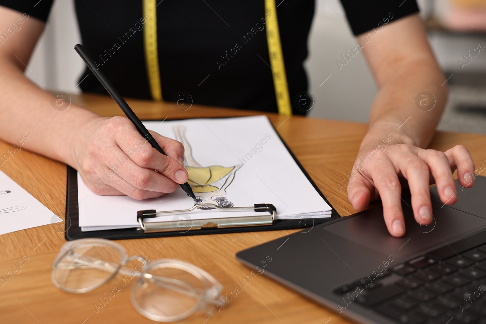 Photo of Fashion designer drawing sketch of beautiful dress at wooden table, closeup