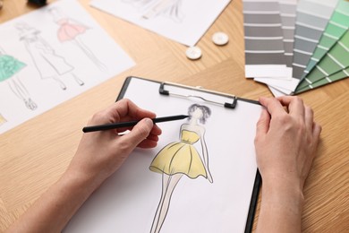 Photo of Fashion designer drawing sketch of beautiful dress at wooden table, closeup