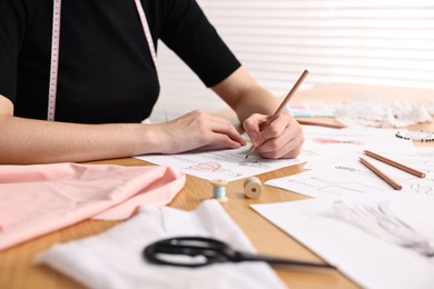 Fashion designer drawing sketch of beautiful dress at wooden table, closeup