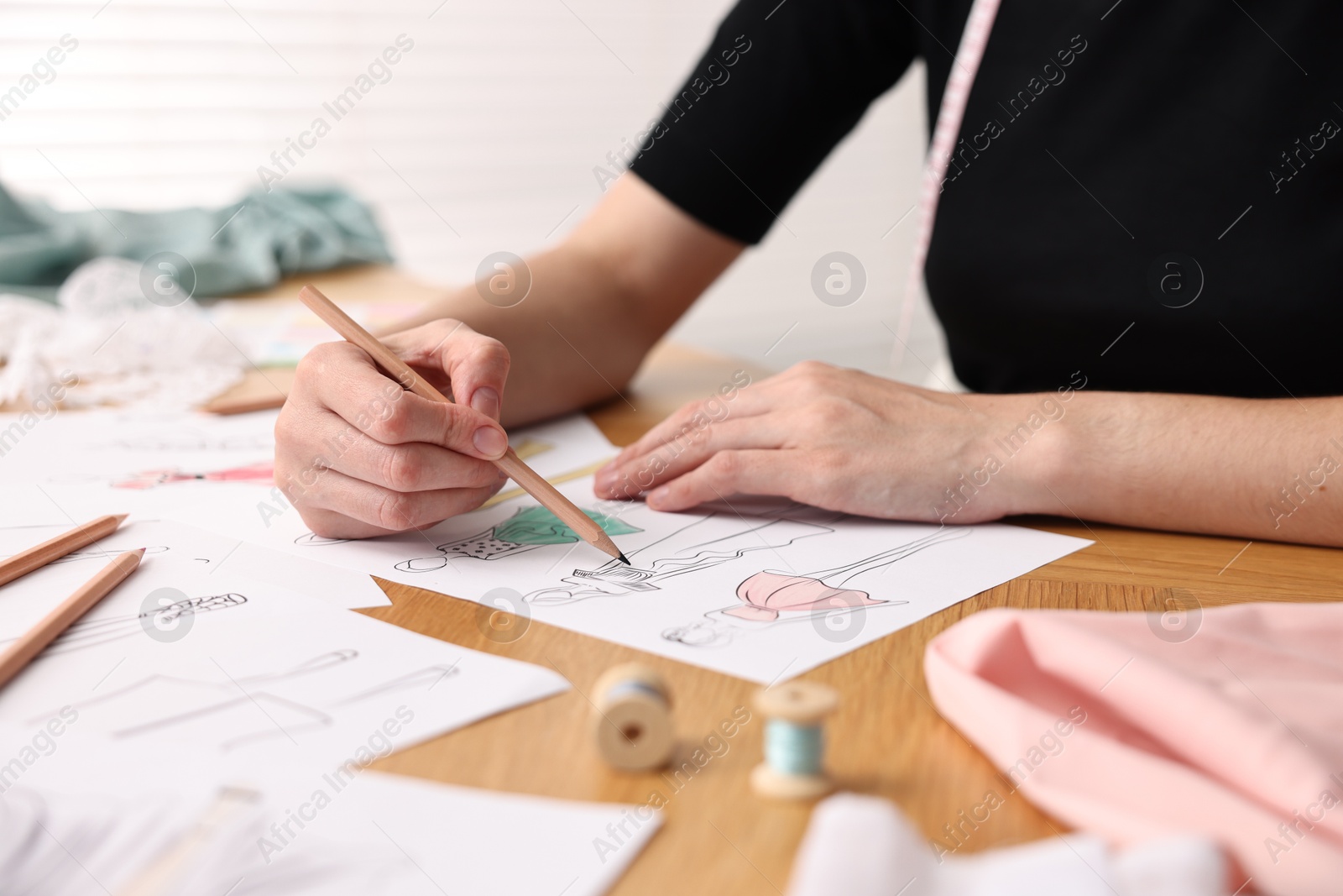 Photo of Fashion designer drawing sketch of beautiful dress at wooden table, closeup