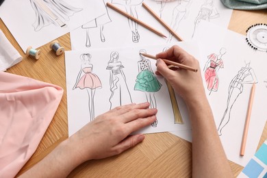 Fashion designer drawing sketch of beautiful dress at wooden table, top view