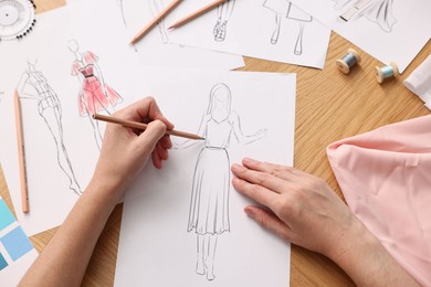 Fashion designer drawing sketch of beautiful dress at wooden table, top view