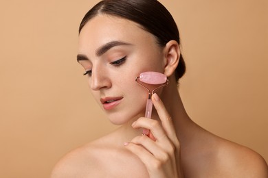 Beautiful young woman doing facial massage with roller on beige background