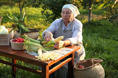 Photo of Senior farmer with different fresh products at wooden table outdoors