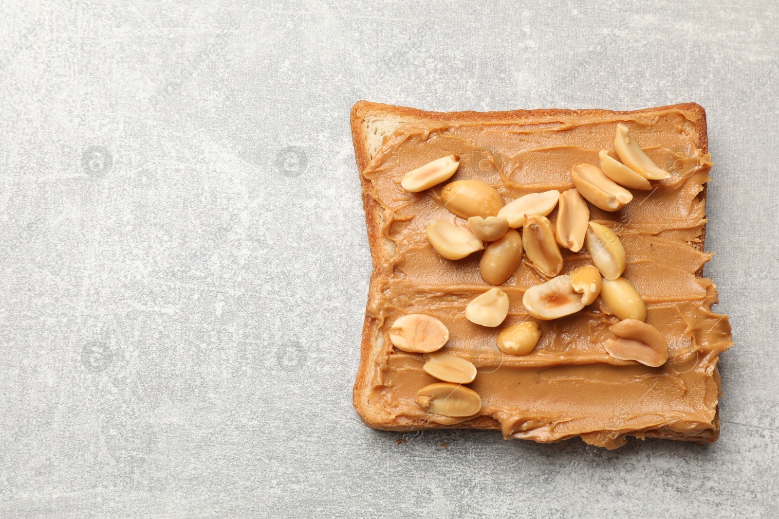 Photo of Tasty sandwich with peanut butter and nuts on grey textured table, top view. Space for text