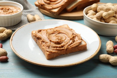 Photo of Tasty sandwich with peanut butter and nuts on light blue wooden table, closeup